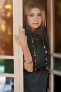 Smiling woman with stylish jewelry and scarf standing at an open door.
