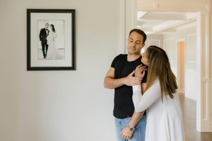 A loving couple embraces indoors beside a framed wedding photo, symbolizing affection and togetherness.