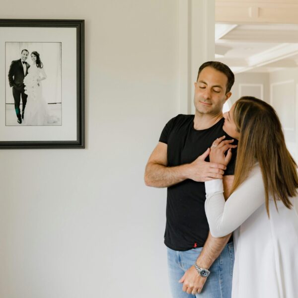 A loving couple embraces indoors beside a framed wedding photo, symbolizing affection and togetherness.